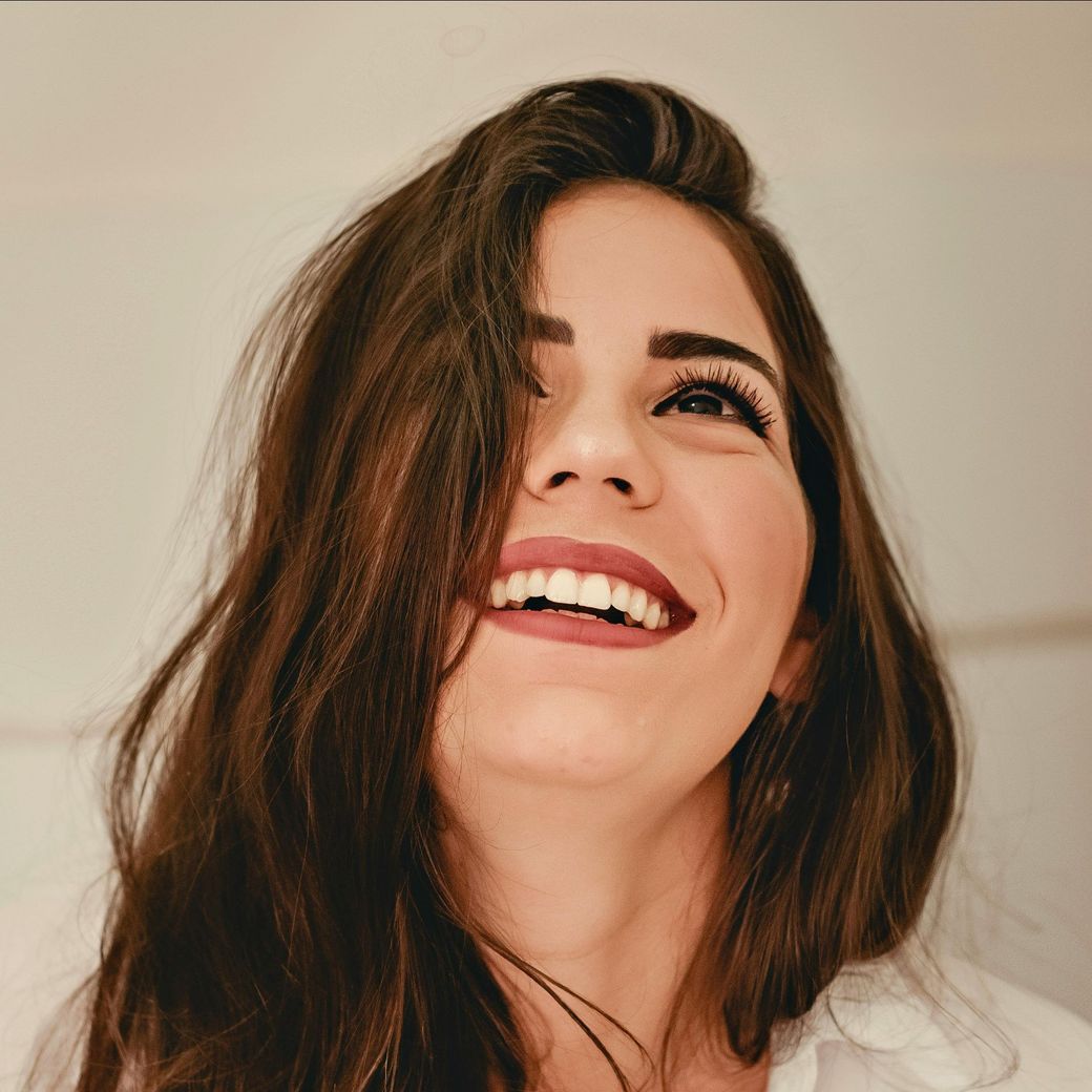 Mujer sonriente con cabello castaño largo sobre un fondo claro.