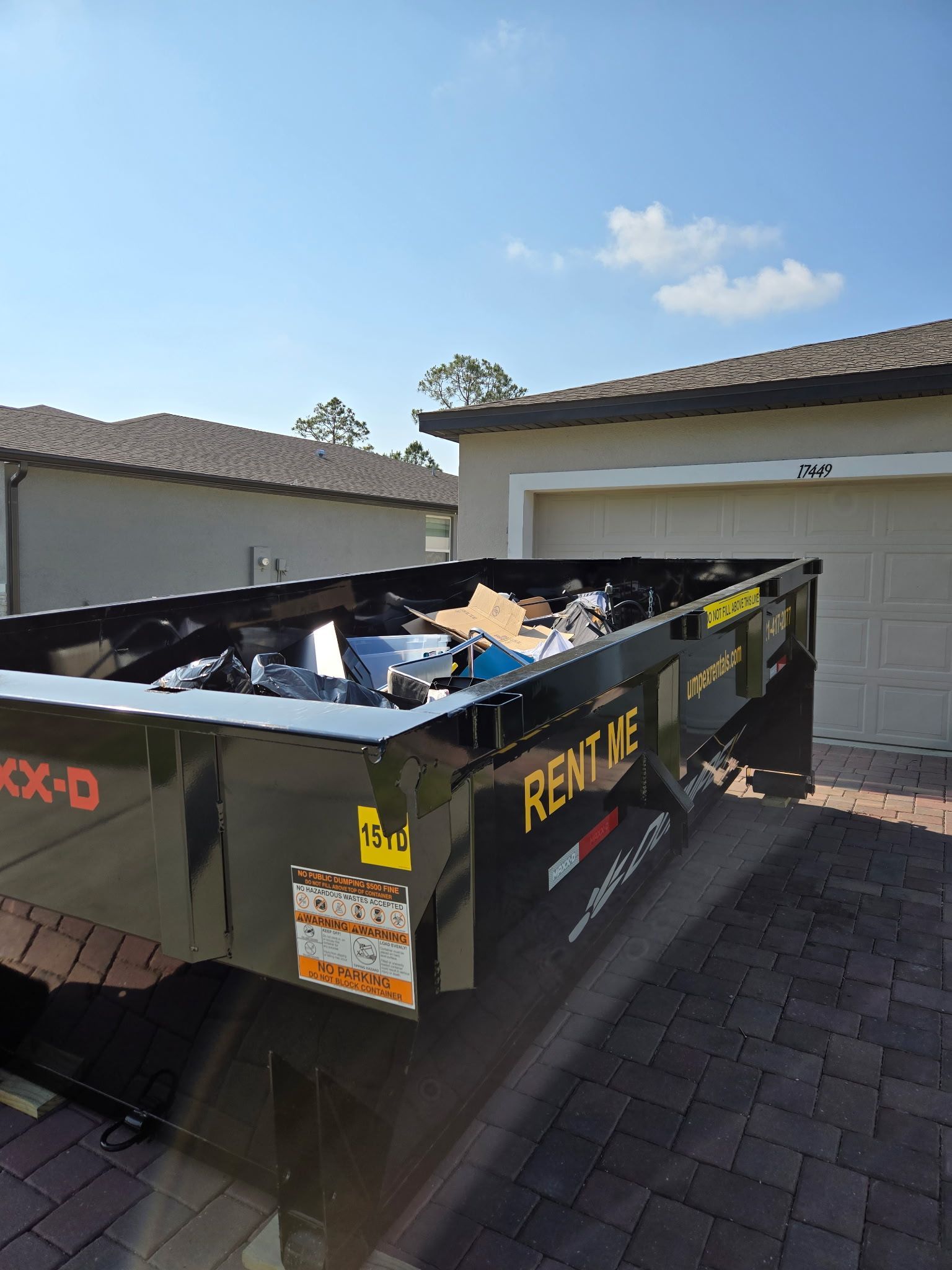 Black construction dumpster labeled “DUMPEX,” filled with debris, parked in a driveway in Winter Park FL