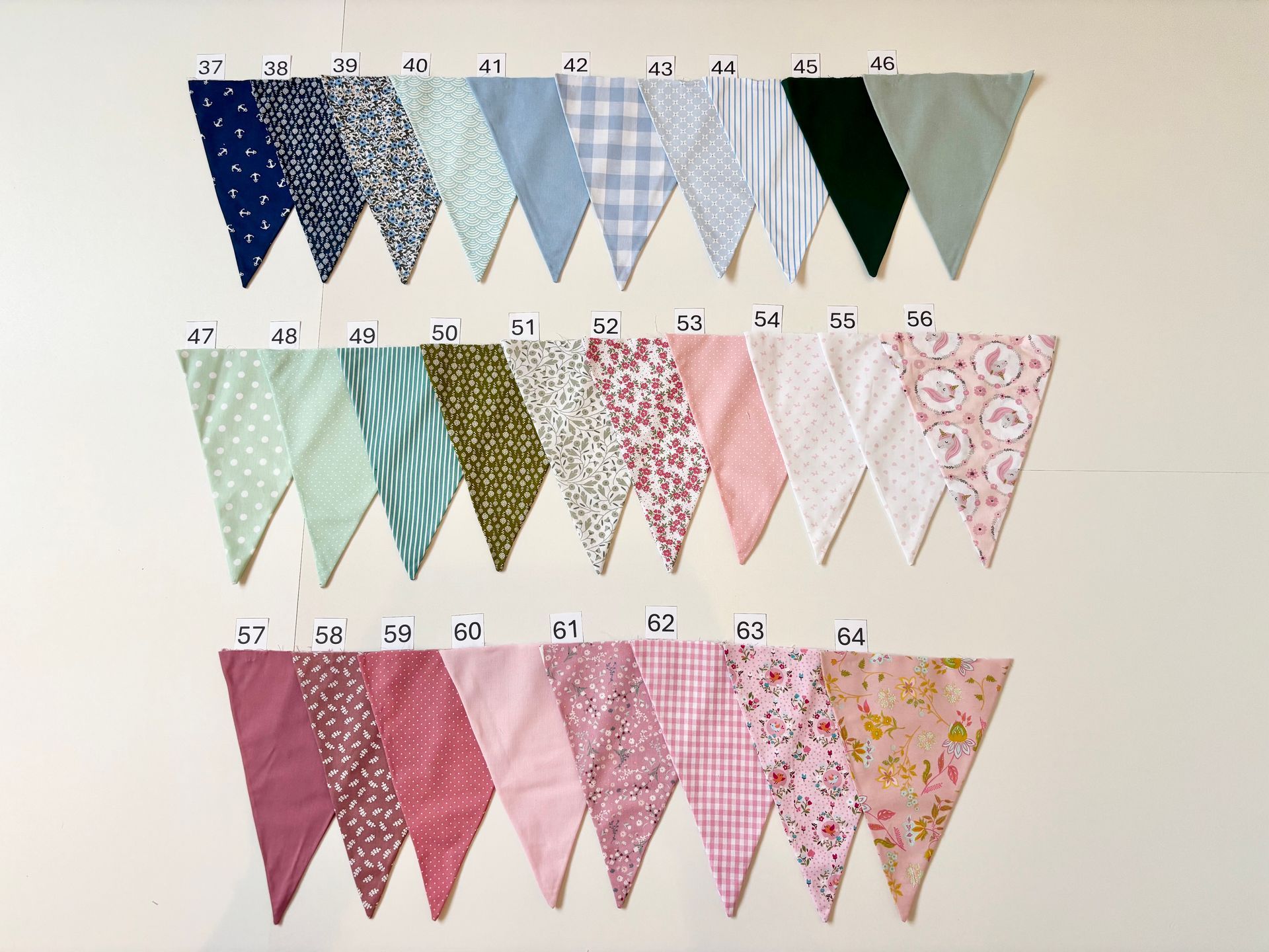 Rijen genummerde decoratieve vlaggetjes in goud-, roze- en witte patronen op een witte muur.