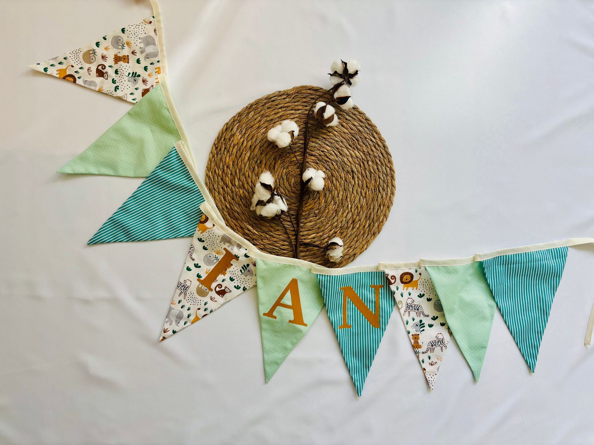 Pastelkleurige slingers met letters in bloemenprint en een geweven nest als middelpunt op een witte achtergrond.