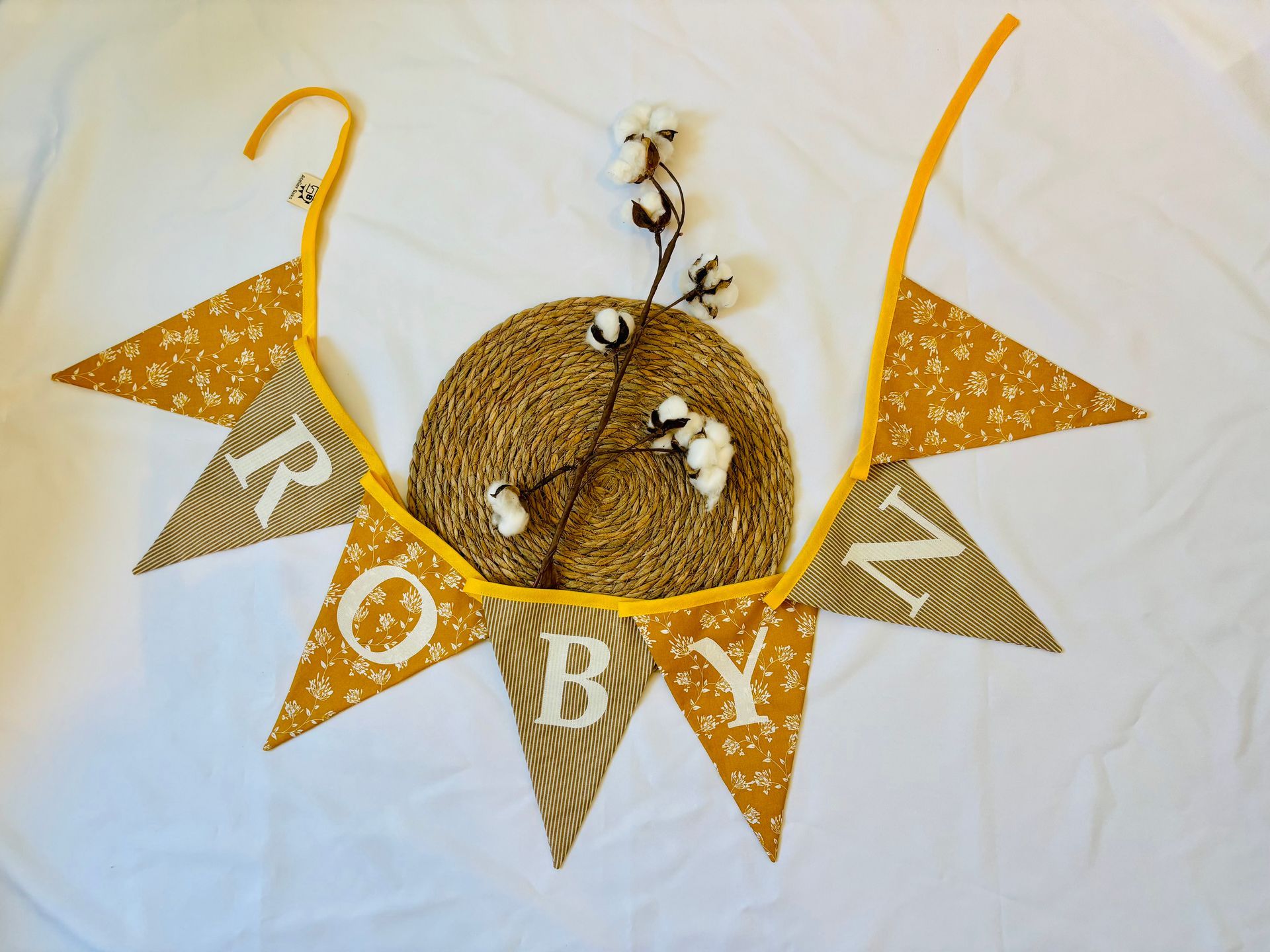 Gouden driehoekige vlaggetjes met witte letters rond een strokrans en gedroogde bloemen op een witte achtergrond.