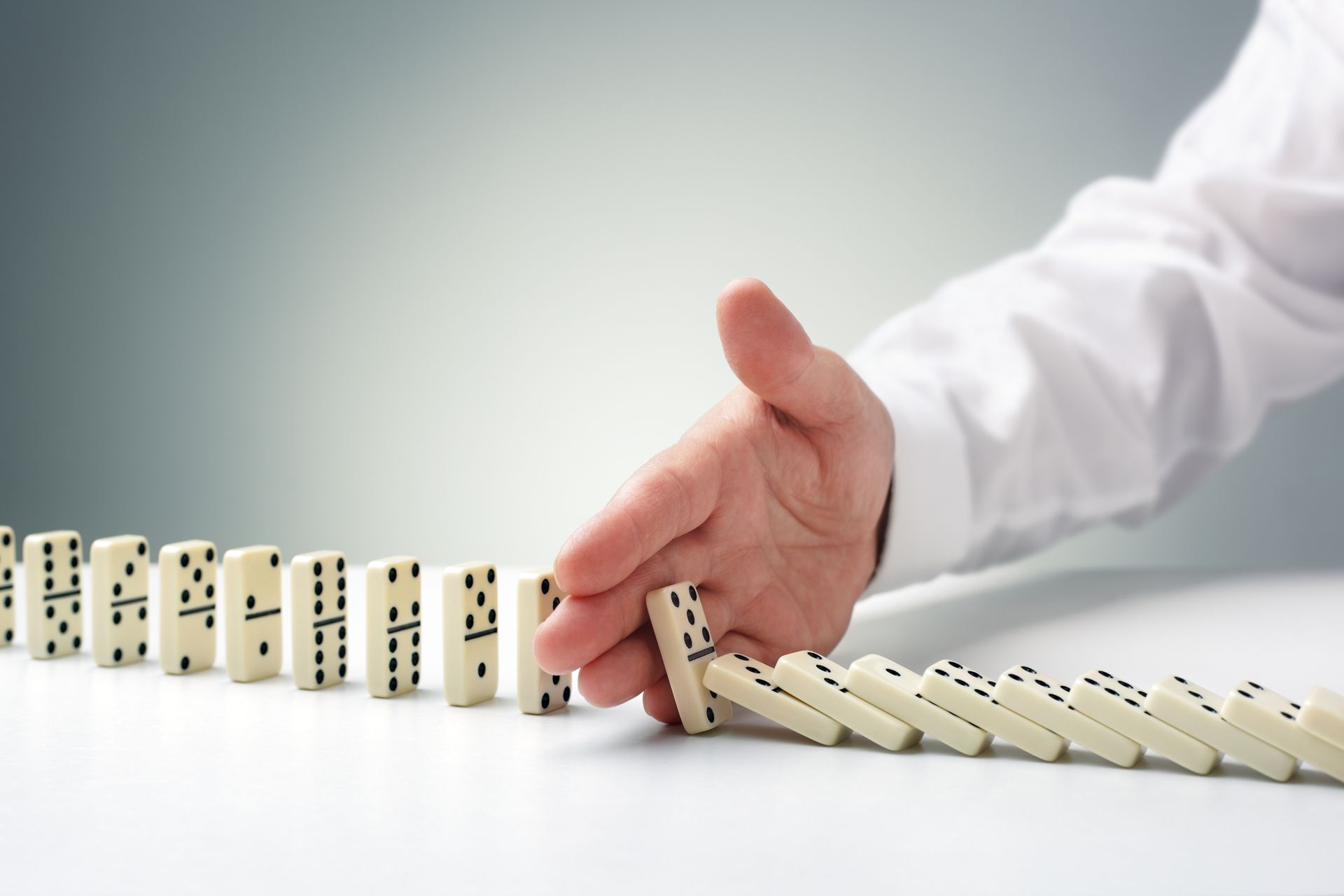 A person 's hand is stopping a row of dominoes from falling