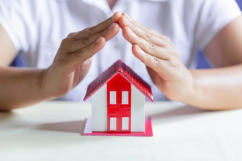 A person is covering a model house with their hands.