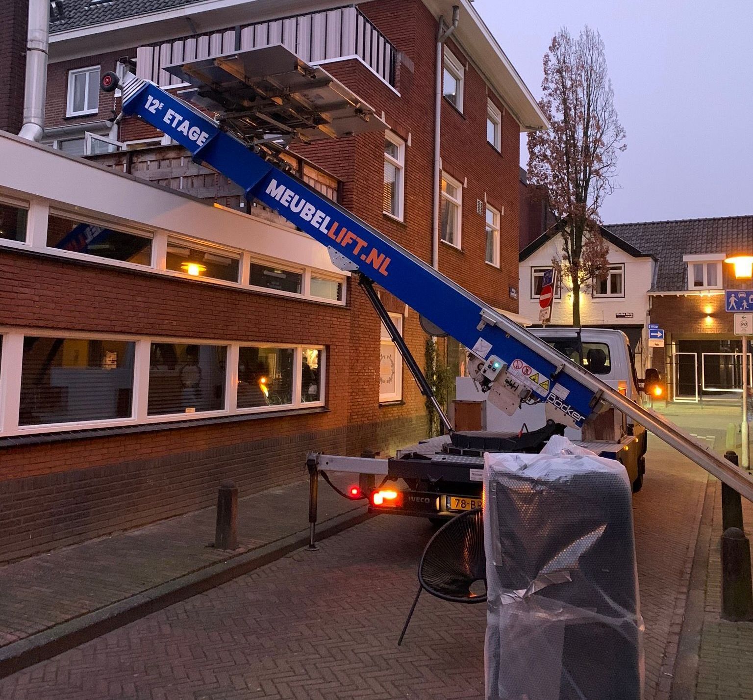 Een meubelheftruck staat geparkeerd voor een bakstenen gebouw