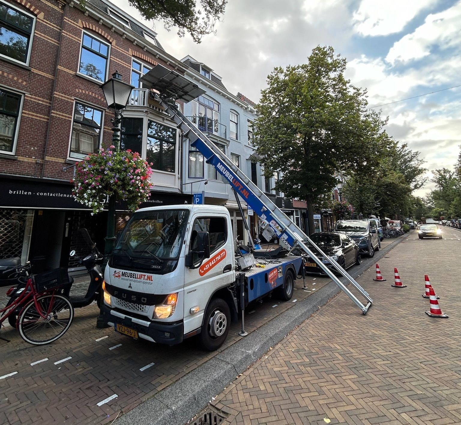 Een witte vrachtwagen met een kraan achterop staat langs de kant van de weg geparkeerd.