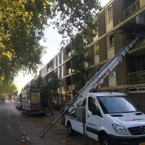 Een witte bestelwagen met een ladder eraan vast staat geparkeerd voor een gebouw