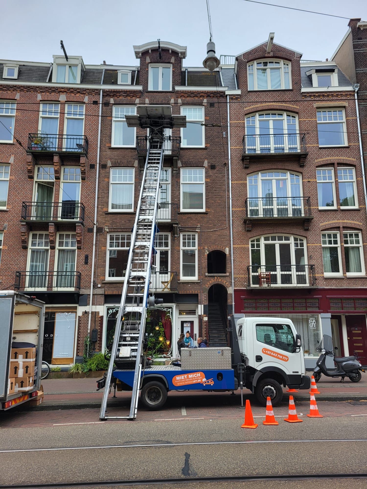 Een vrachtwagen met daaraan een ladder staat geparkeerd voor een bakstenen gebouw