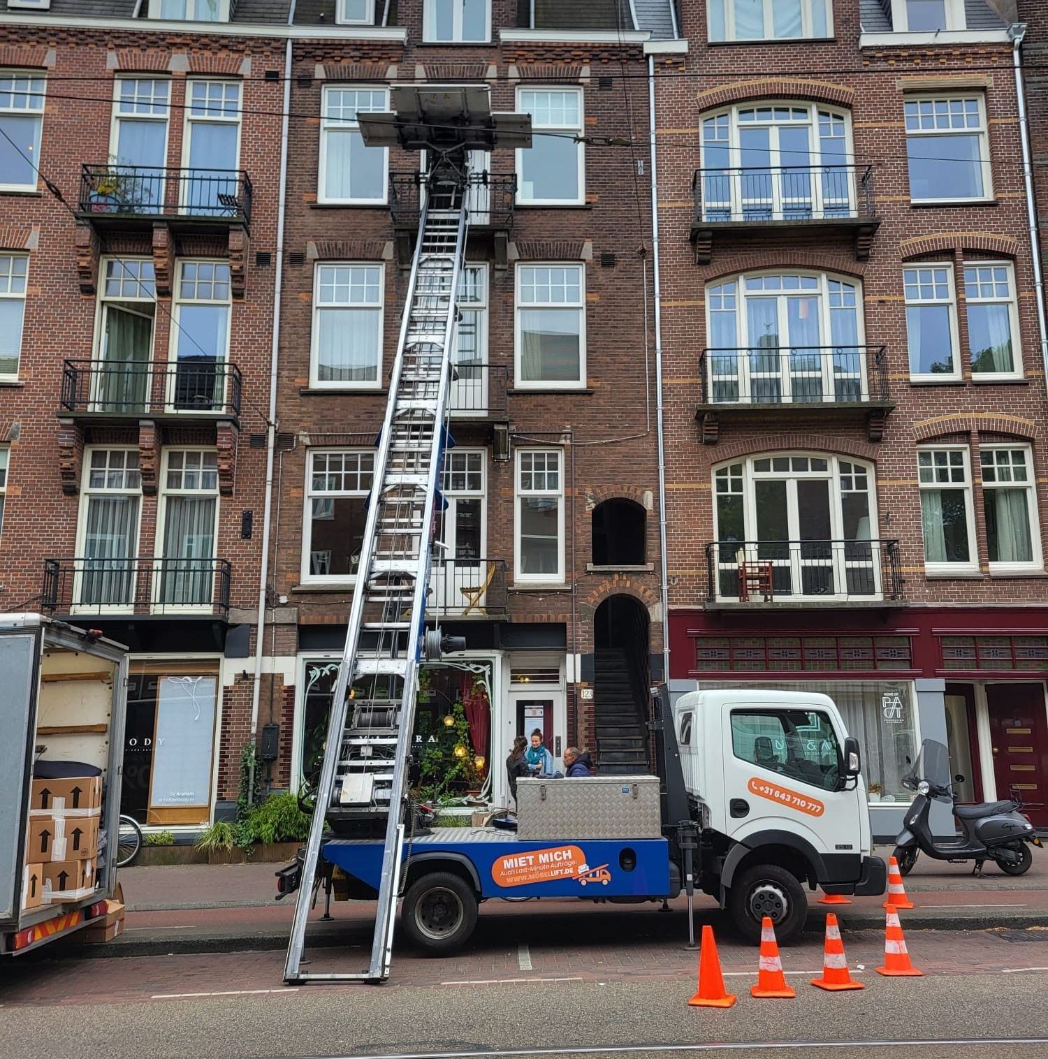 Een vrachtwagen met daaraan een ladder staat geparkeerd voor een bakstenen gebouw