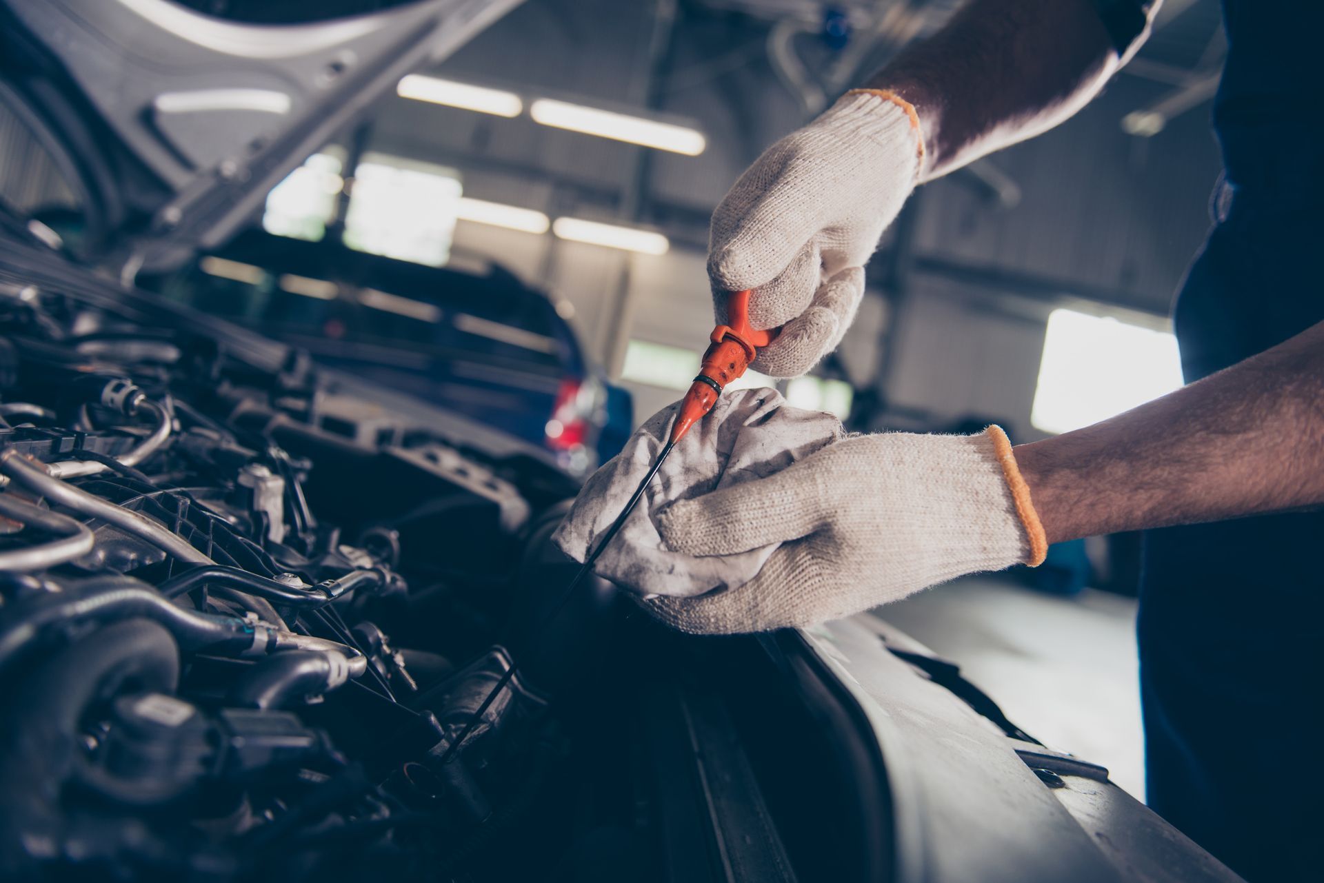 Mechanic at local auto repair shop checks engine oil using dipstick and cloth in well-lit garage.