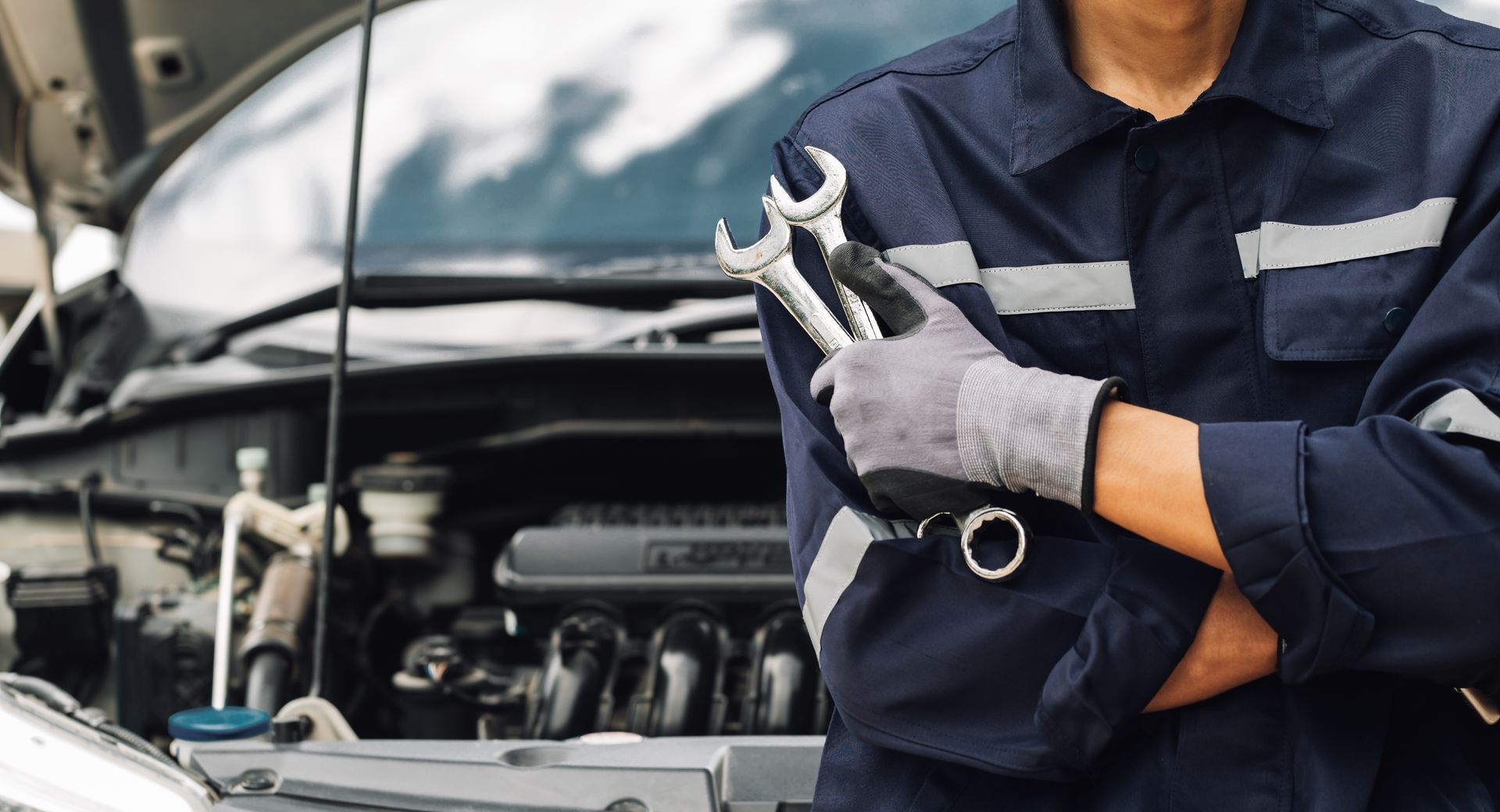 Professional holding wrenches near car engine bay for reliable auto repair service.