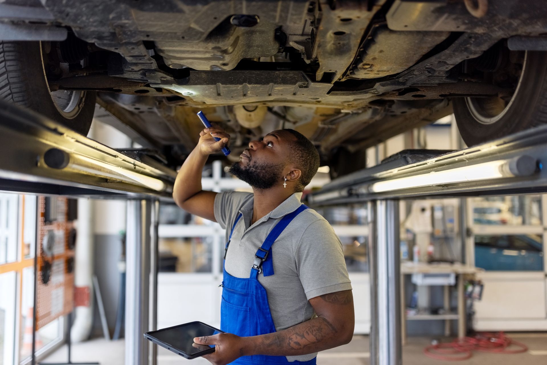 Mechanic checks under car with flashlight and tablet.