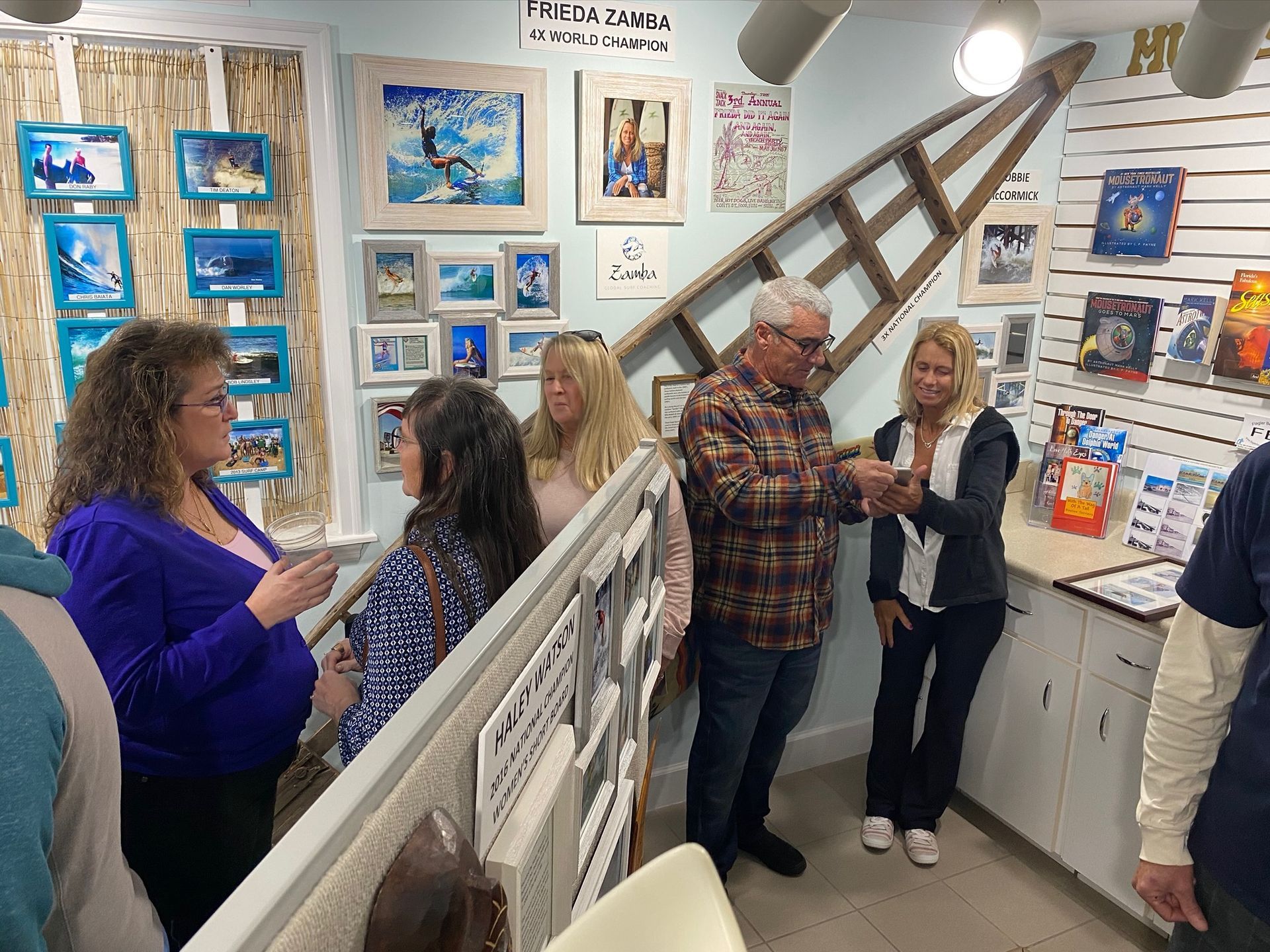 People browsing artwork in a bright gallery with blue paintings and a leaning ladder display