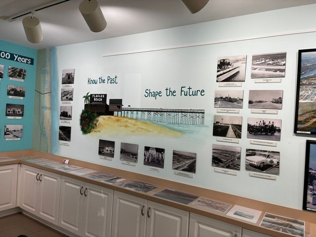 Museum exhibit wall with historical photos, maps, and a “Shape the future” display above white cabinets