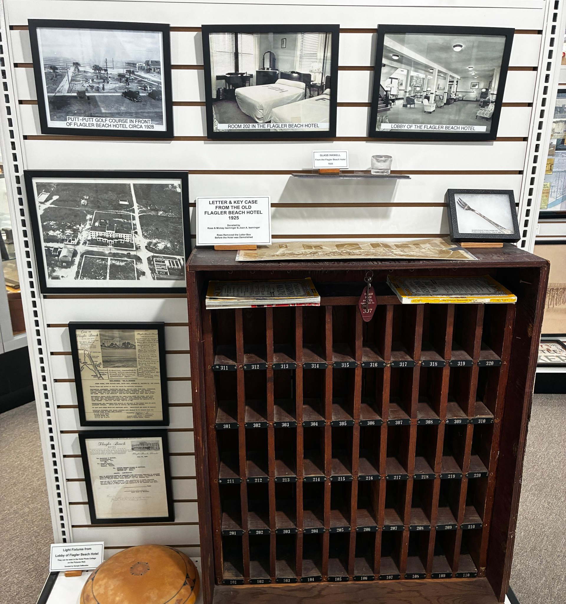 Antique wooden mail sorter beneath framed black-and-white photos and documents on a wall display.