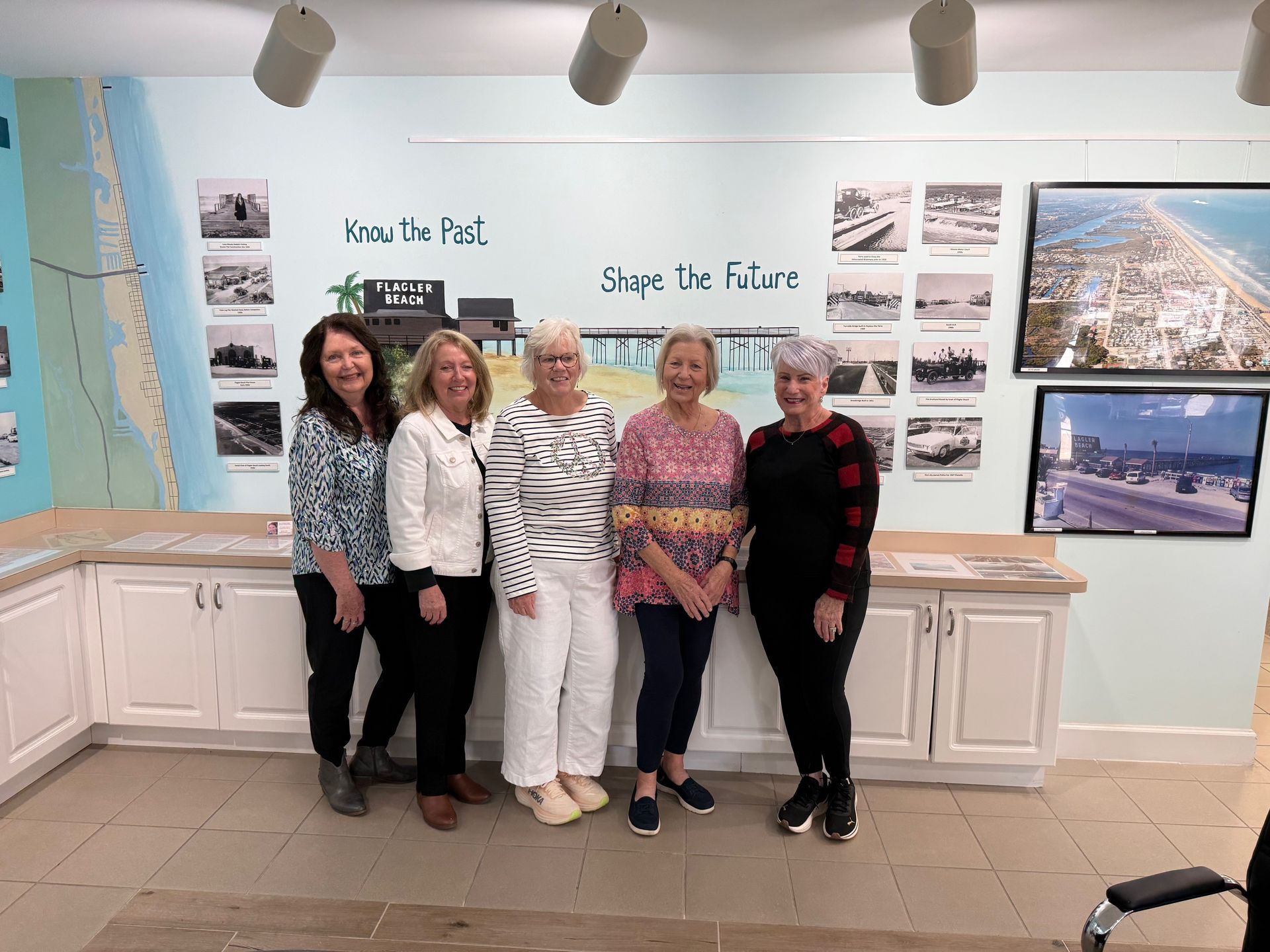 Five people posing in a bright gallery beside wall text and coastal photos.