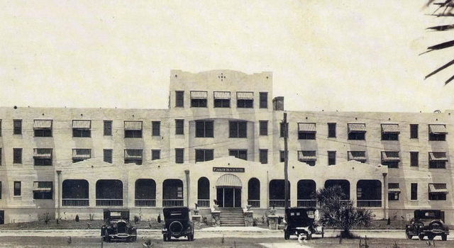 Historic sepia-toned building facade with arched windows and parked cars in front