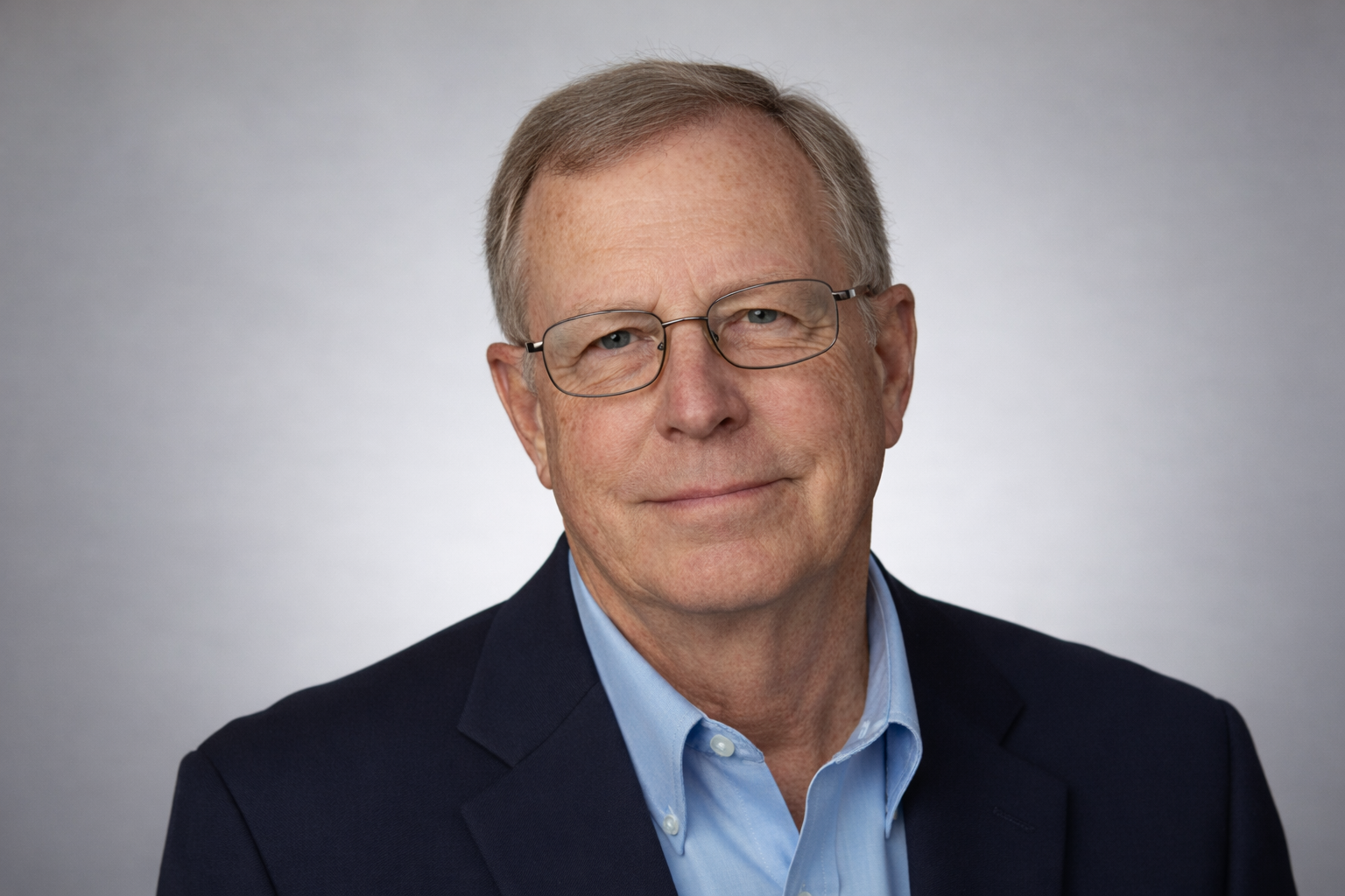 Portrait of a man in glasses wearing a dark blazer and light blue shirt against a gray background