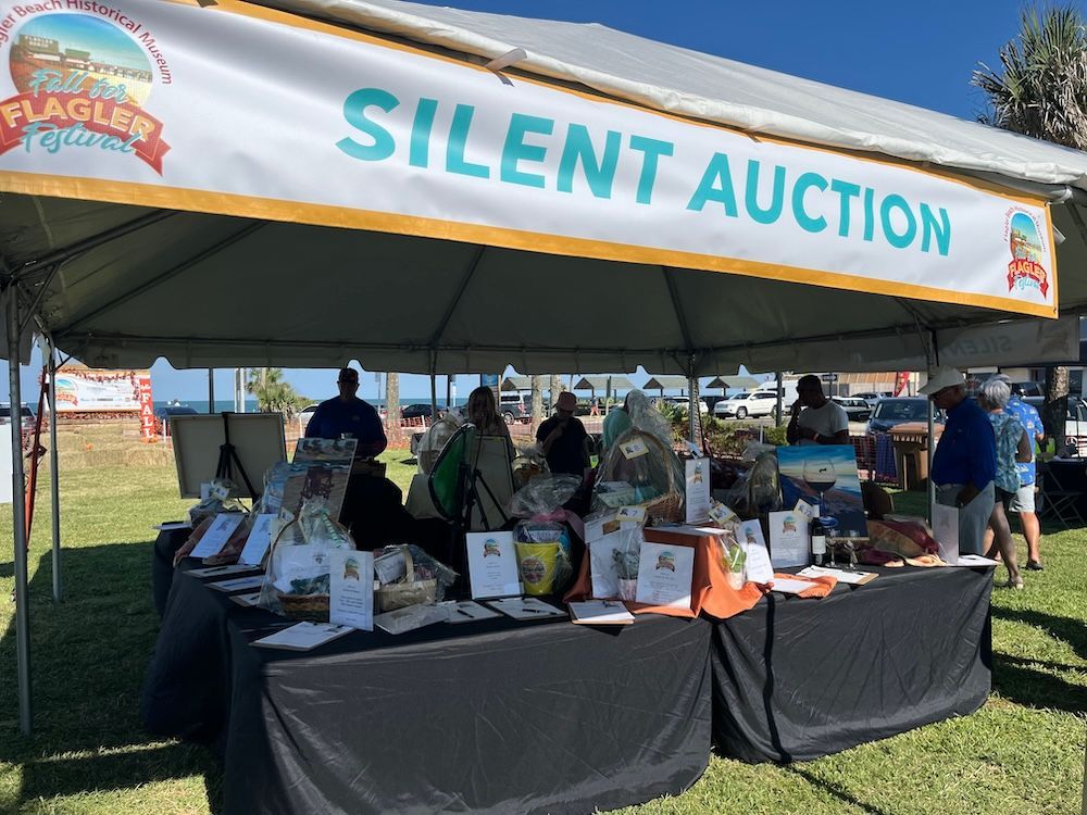 Silent auction booth under a tent with tables of items and volunteers at an outdoor event