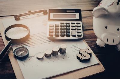 Calculator, magnifying glass, coins, and piggy bank on a desk, suggesting saving and budgeting