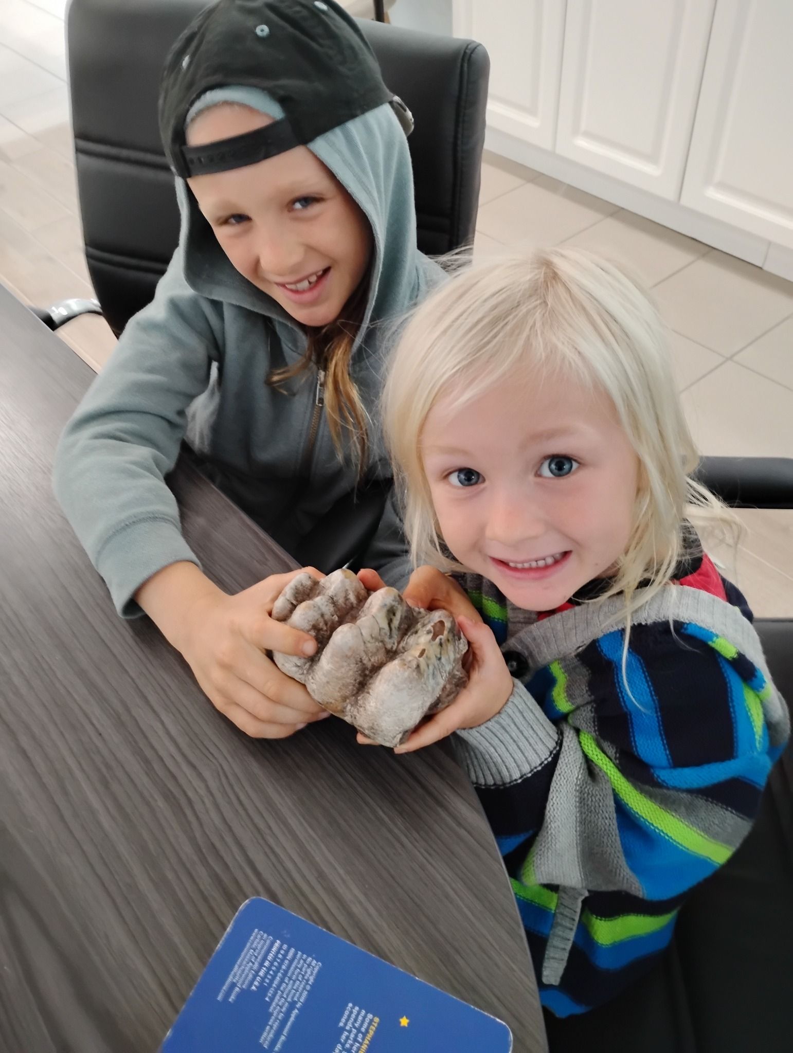 Two children smiling at a table, gently holding a small bunny indoors.