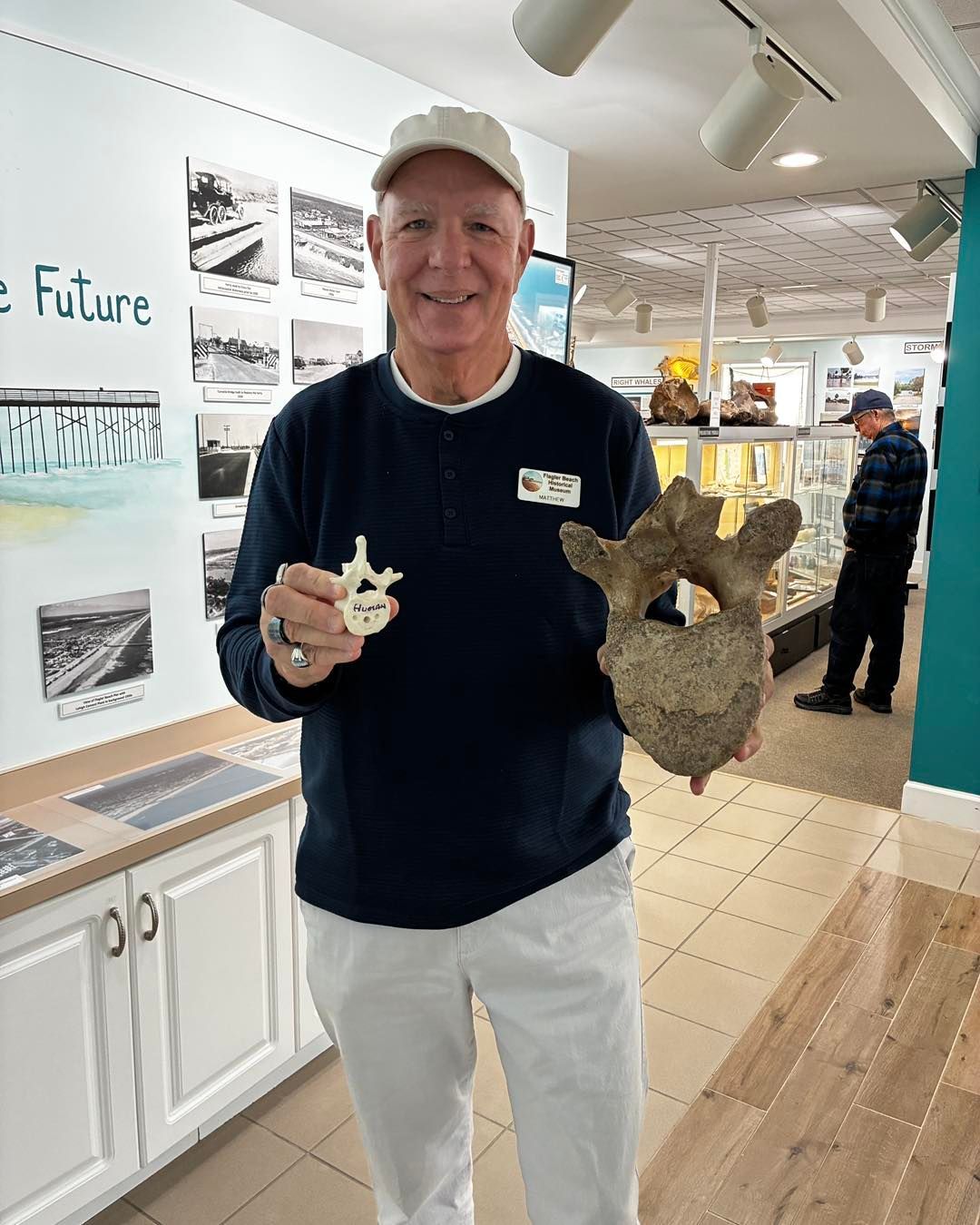 Man in a shop holding two coral-like sculptures, standing beside a display wall with beach photos and text.