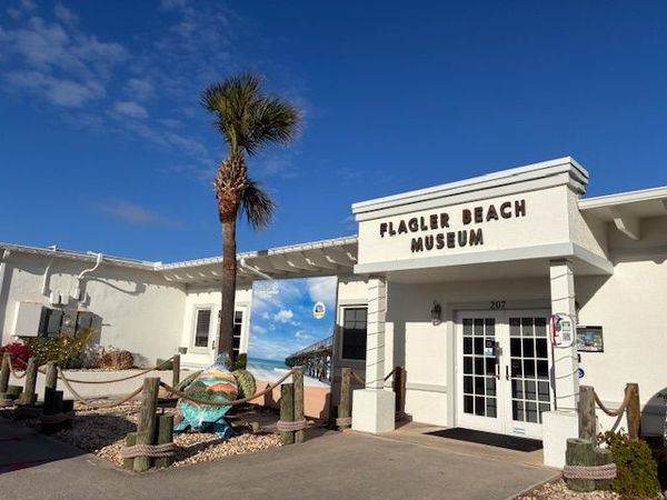 Flagler Beach Museum exterior with white facade, palm tree, and blue sky