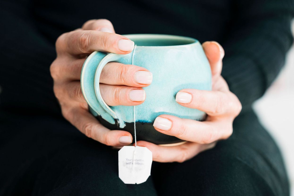 A woman is holding a cup of tea with a tea bag in her hand.