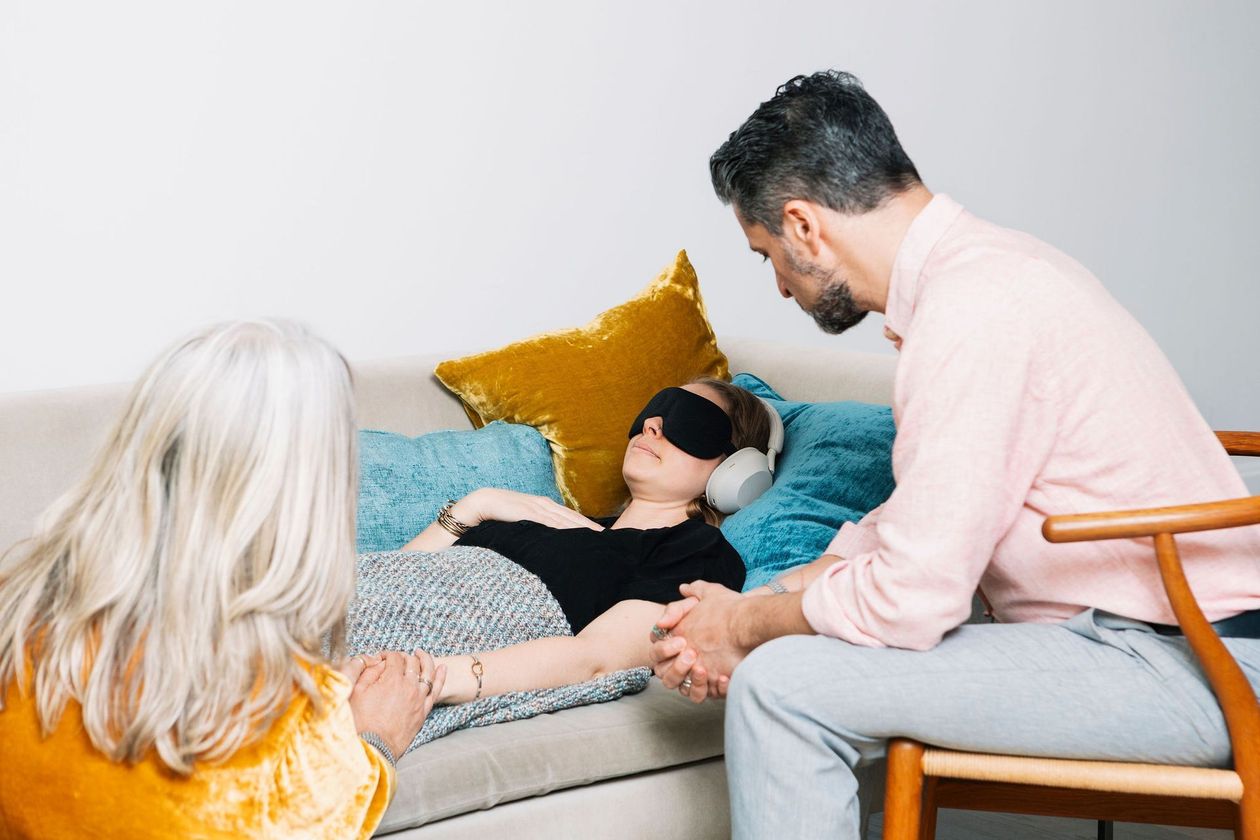 A man is sitting next to a woman laying on a couch.