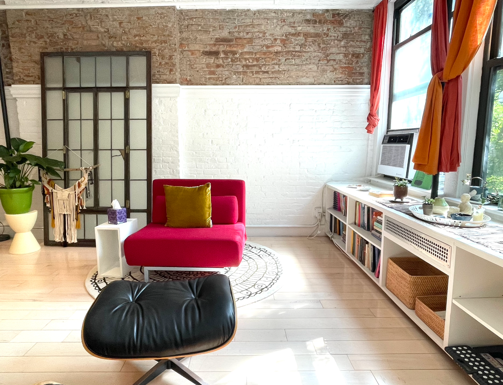 A living room with a red chair and a black ottoman