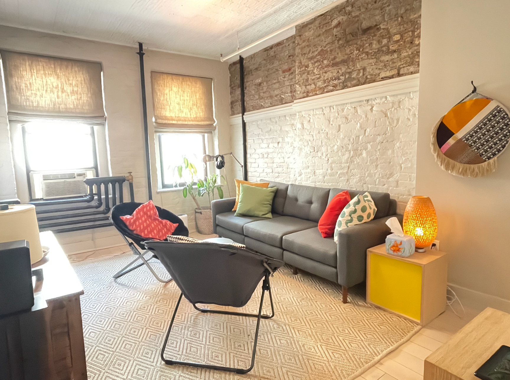 A living room with a couch and chairs and a brick wall.