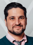 A man with a beard is wearing a pink shirt and tie.