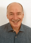 A bald man with a mustache is smiling for the camera while wearing a blue shirt.