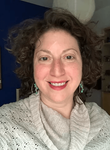 A woman with curly hair and earrings is smiling for the camera.