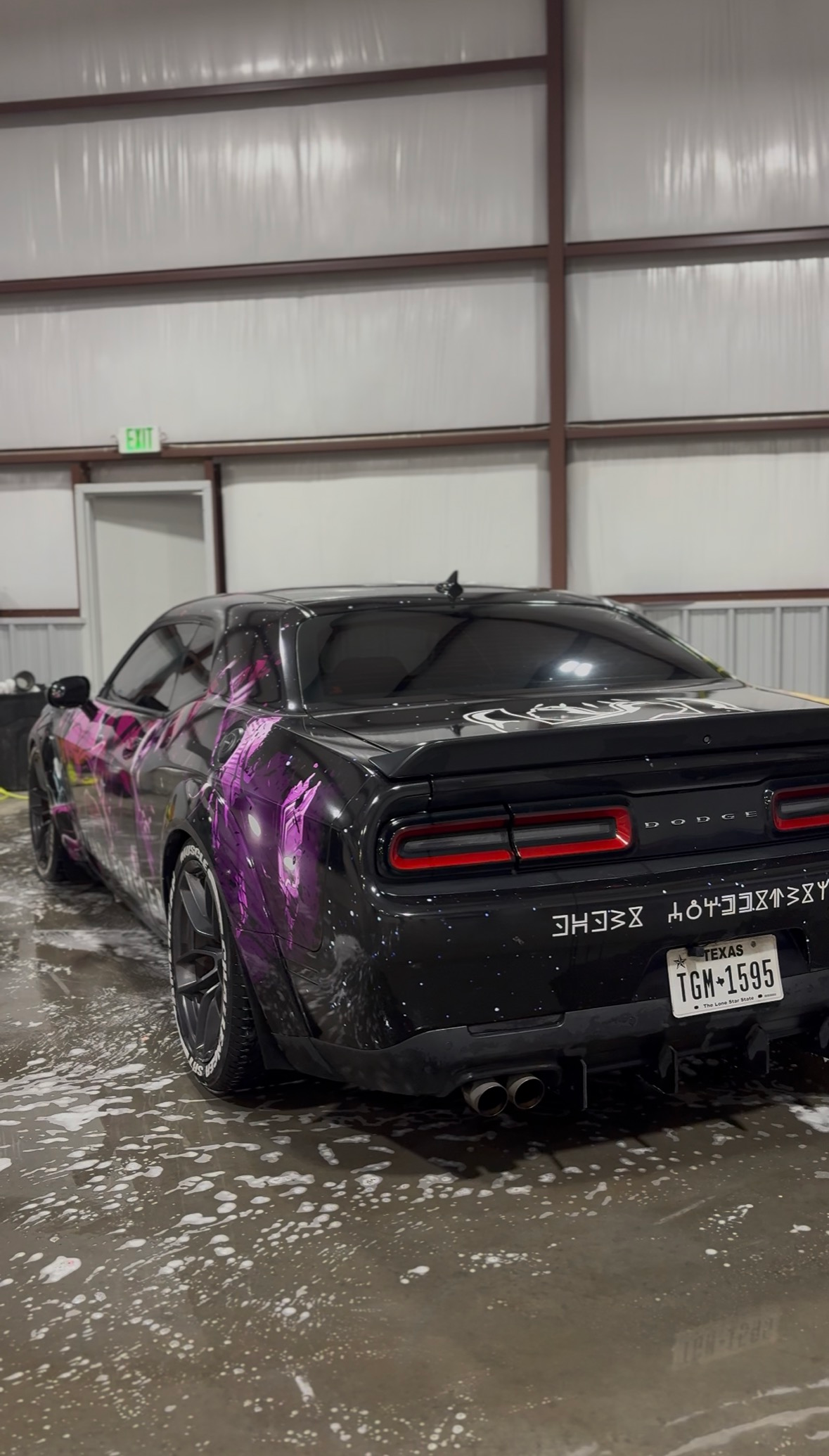 Black sports car with purple paint splashes inside a wet garage, surrounded by water on the floor