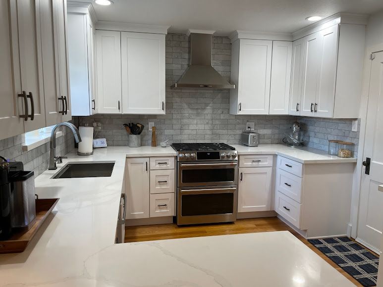 A kitchen with white cabinets , a stove , a sink , and a hood.
