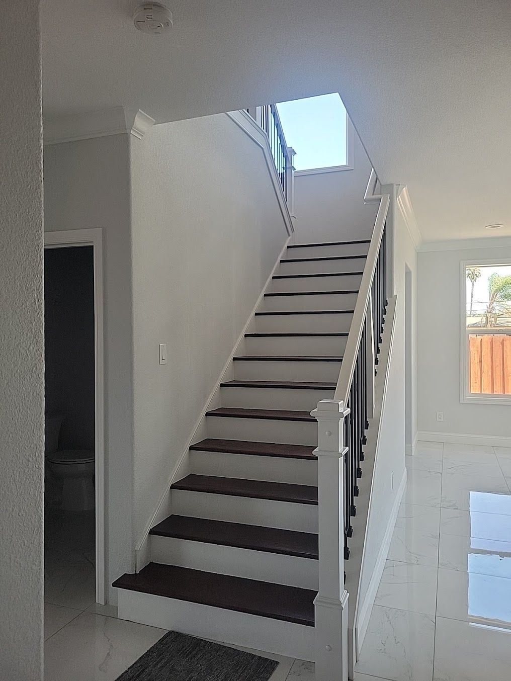 A white staircase with brown steps leading up to the second floor of a house.
