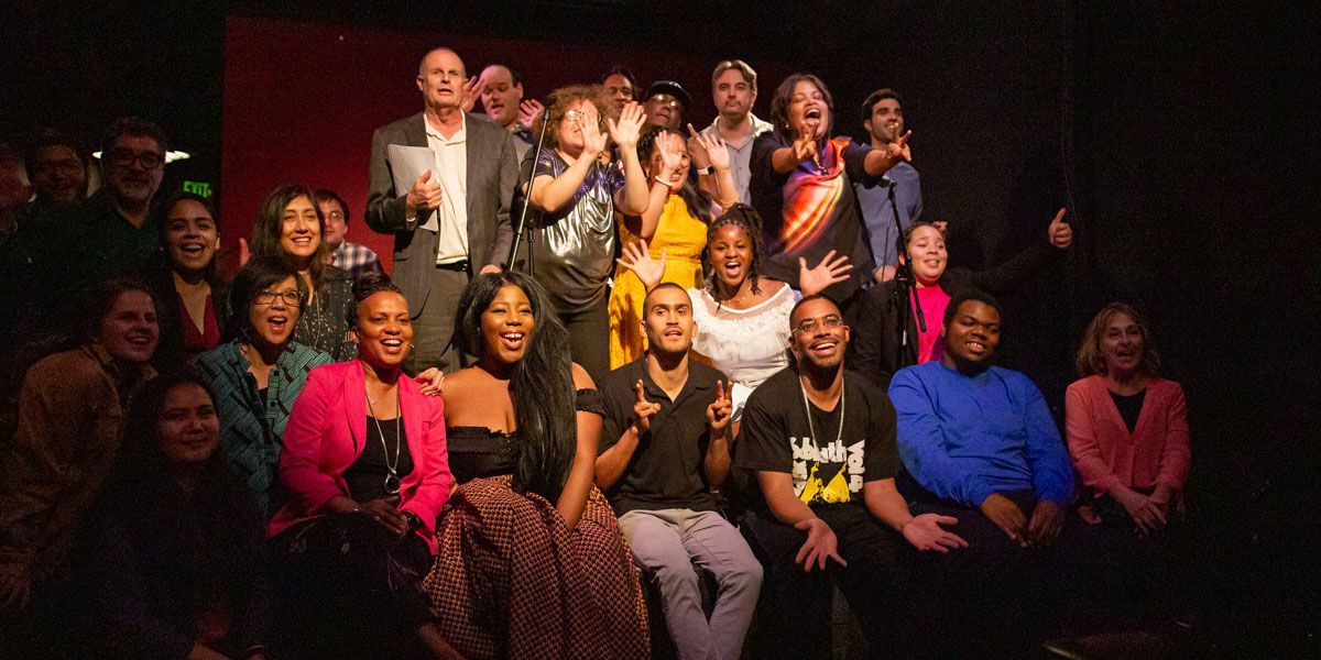 Group of diverse people, mostly smiling, posing together in what appears to be a theater.