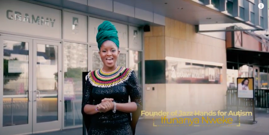 Woman in teal head wrap and beaded necklace stands outside building with