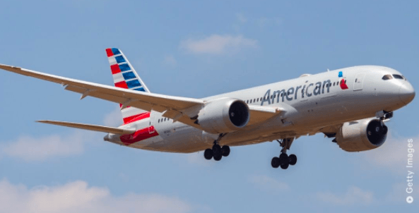 American Airlines airplane in flight against a blue sky, with landing gear down.