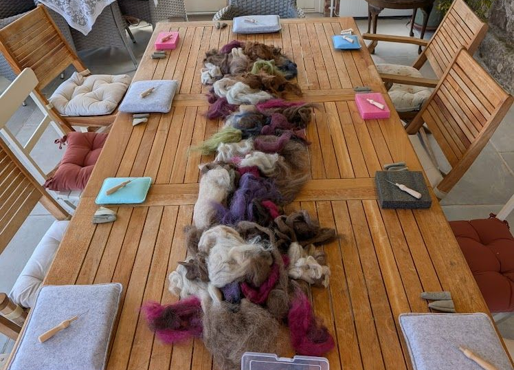 Wool fibers laid out on a wooden table with chairs and cushions around it