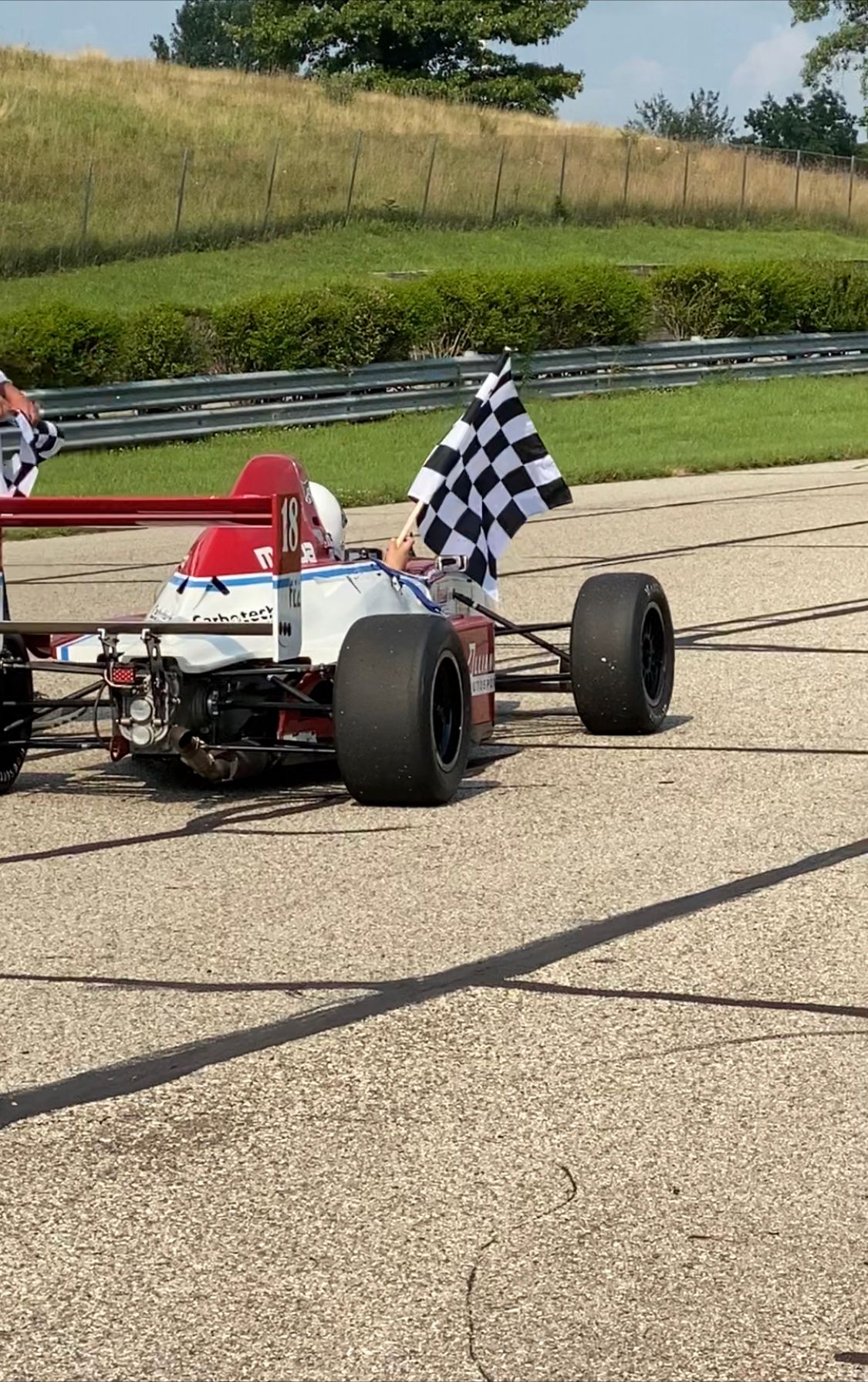 Small race car with a checkered flag on a paved track beside grass embankments