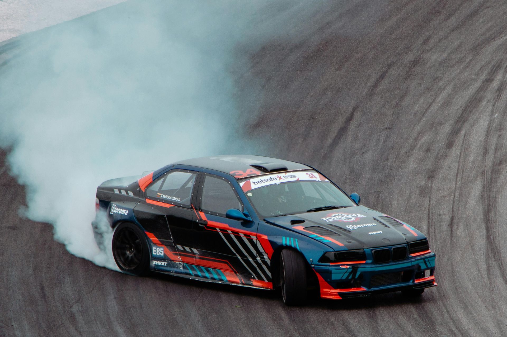 Black and red drift car sliding on a track, trailing smoke around a sharp turn
