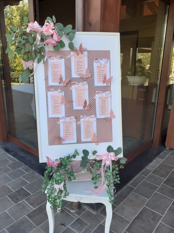 La planimetria dei posti a sedere è esposta su un cavalletto, decorata con fiori e farfalle.