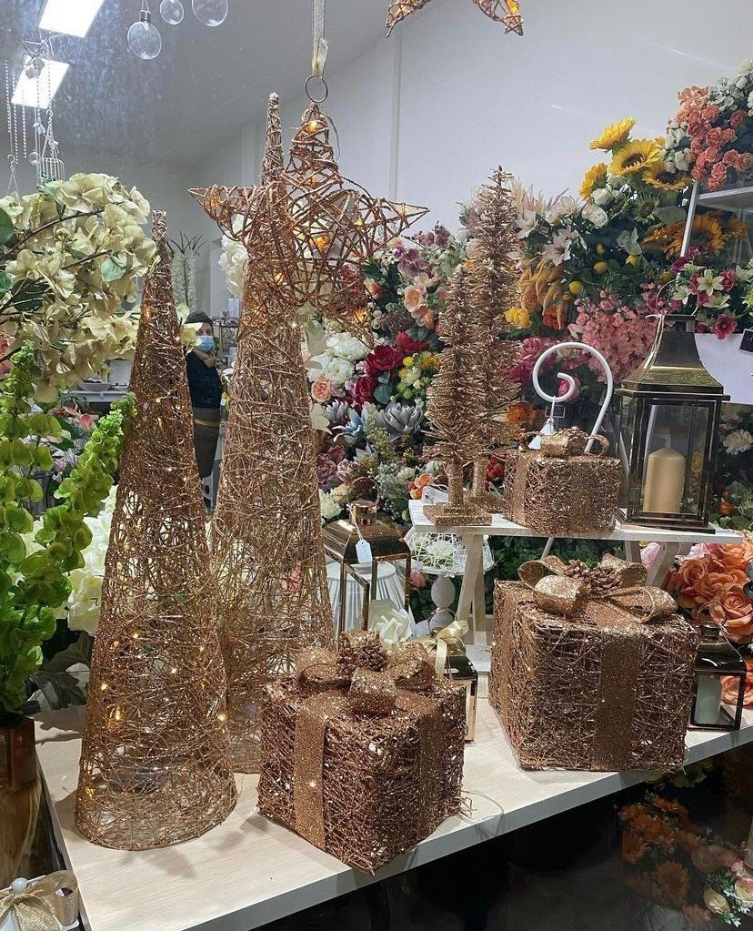 Decorazioni natalizie scintillanti color oro rosa, tra cui alberi e scatole regalo, in un negozio.