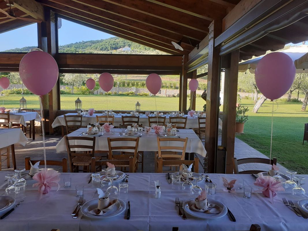 Allestimento per feste all'aperto: tavoli apparecchiati con palloncini rosa e decorazioni.