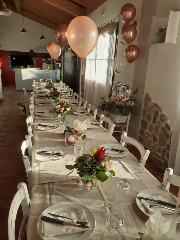 Lungo tavolo apparecchiato per una festa. Palloncini color oro rosa decorano la sala.