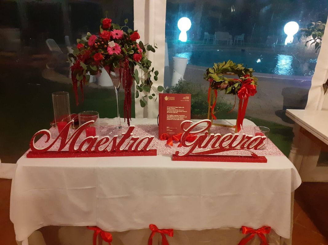 Tavolo decorato con accenti rossi per un evento. Le composizioni floreali affiancano due nomi in corsivo rosso: