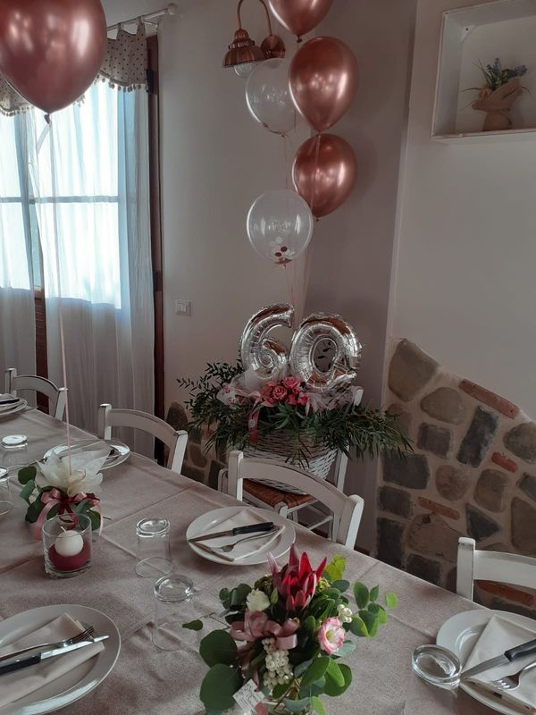 Tavolo apparecchiato per una festa con palloncini color oro rosa e centrotavola floreale per celebrare il 60° compleanno.