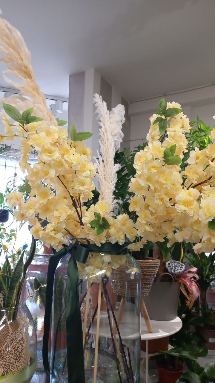 Composizione floreale gialla in un vaso trasparente con erba della pampa e foglie verdi.