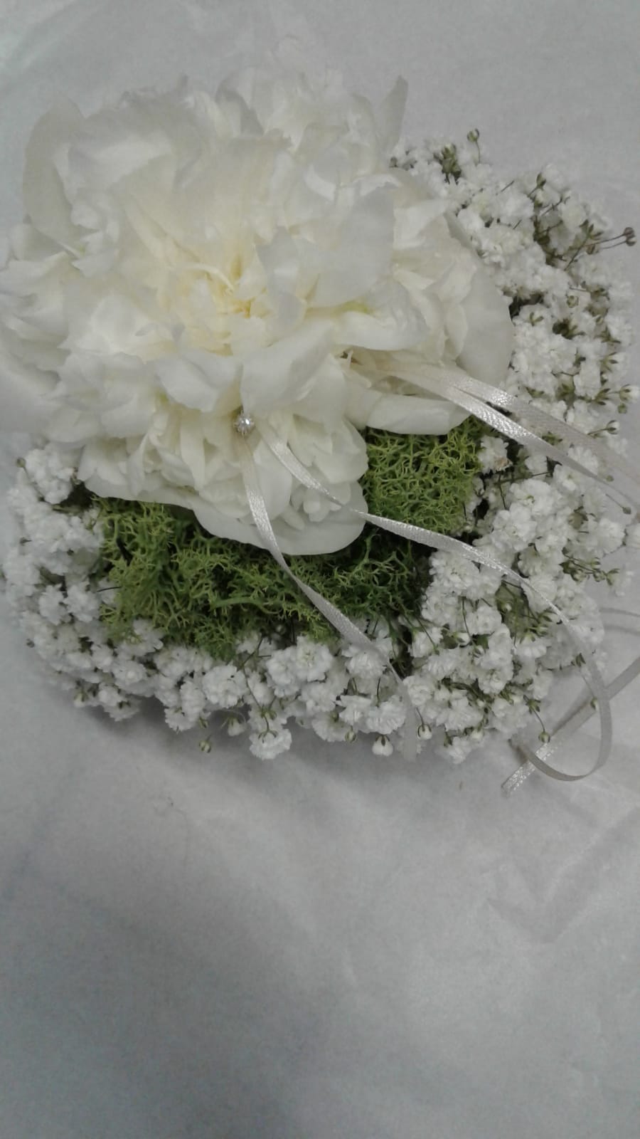 Cuscino per fedi nuziali: fiore di stoffa bianco su muschio verde, circondato da gypsophila bianca.